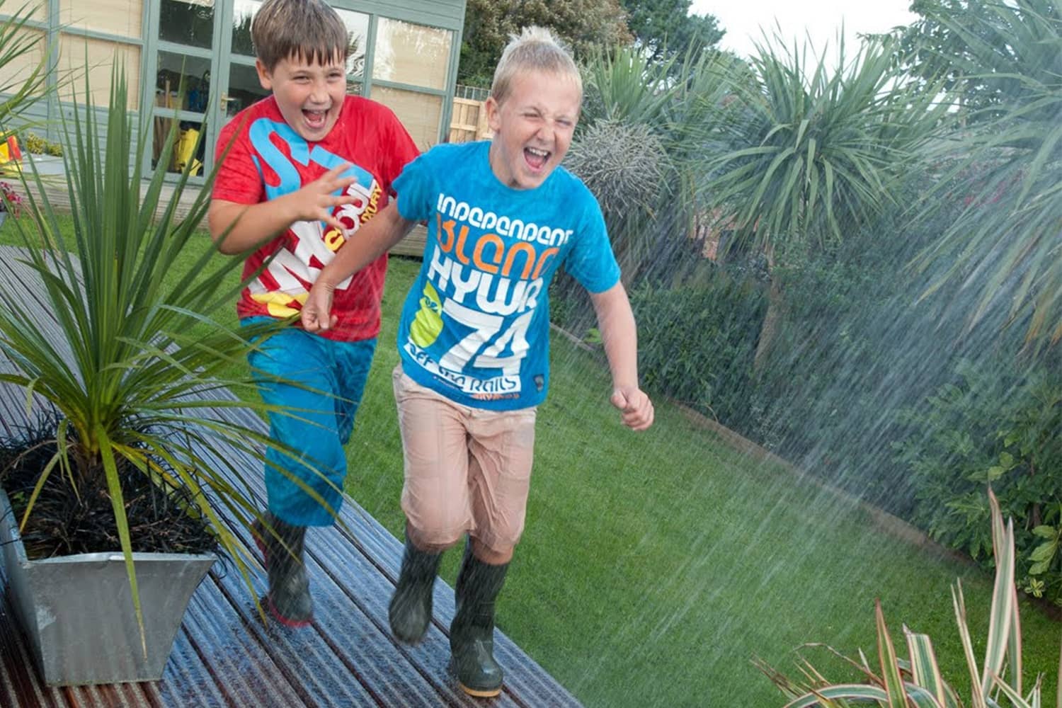 Children running on anti-slip decking through garden sprinkler